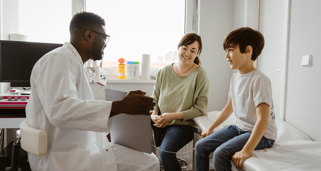 A doctor speaks with a mother and young boy seated together during a pediatric appointment.
