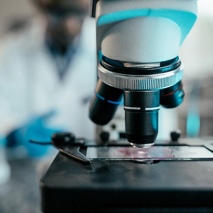 Image of a microscope, and a scientist working in the background.